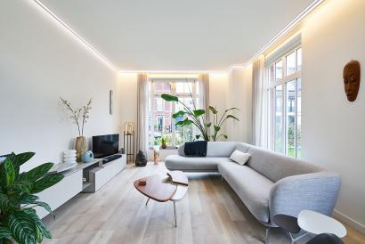 Woonkamer in Scandinavische stijl met witte muren, houten vloer en planten. Mat wit Plameco spanplafond met led-strips.